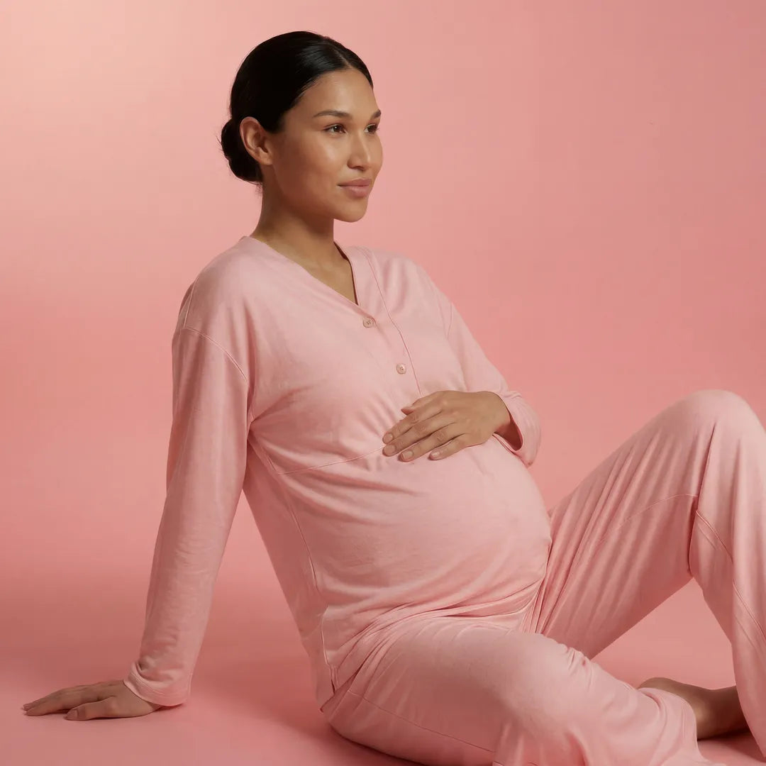 Pink maternity nursing pyjama set button V-neck top and trousers, floor seated studio shot