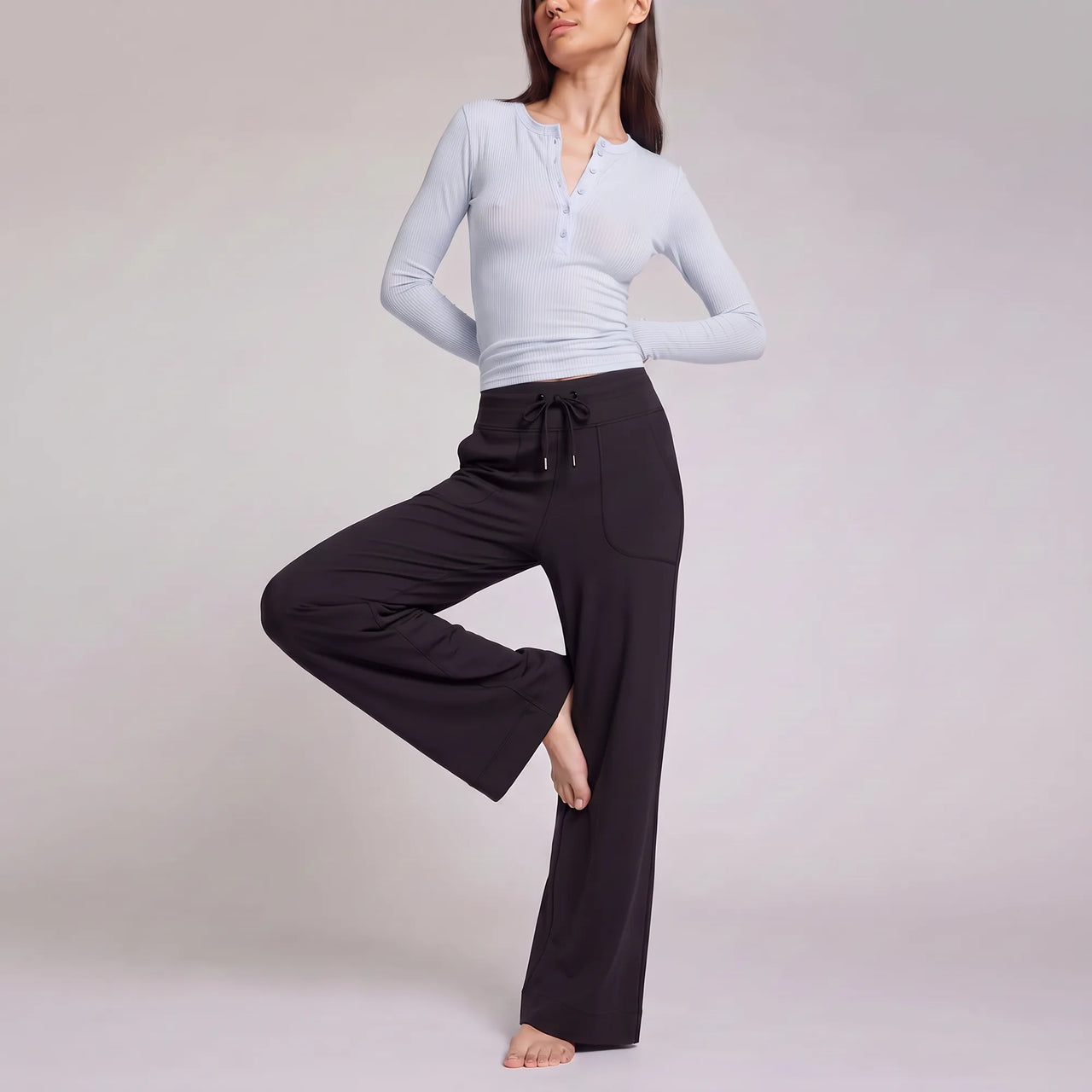 A woman modeling a light blue long-sleeve henley top and black wide-leg drawstring pants against a plain light gray studio background.