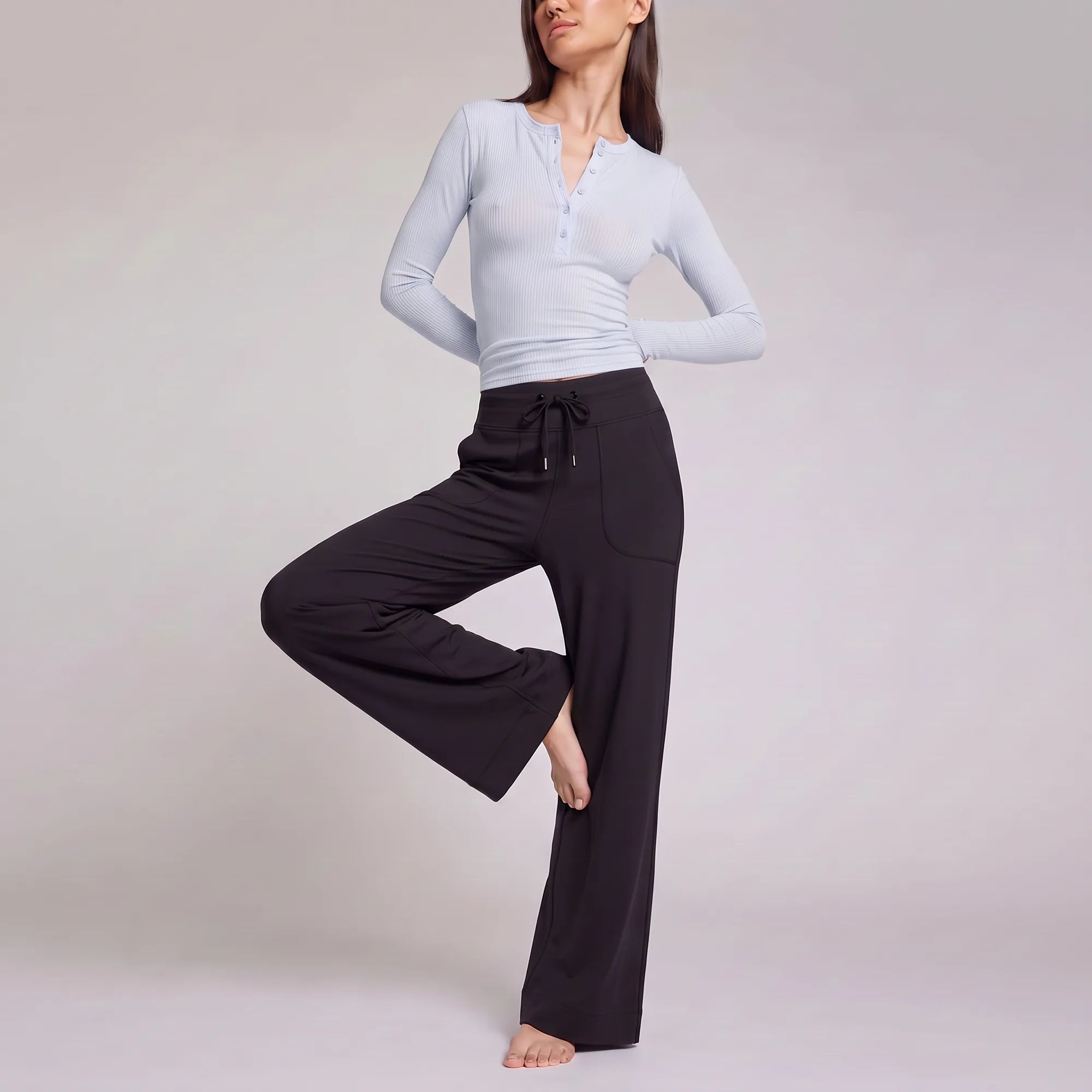 A woman modeling a light blue long-sleeve henley top and black wide-leg drawstring pants against a plain light gray studio background.