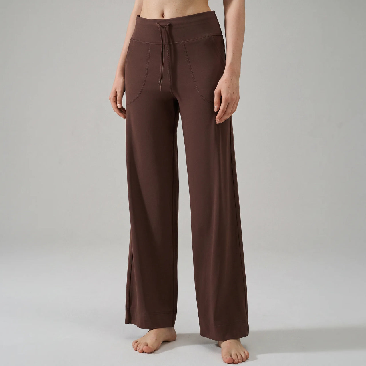 A model wearing brown wide-leg drawstring pants, shown from the waist down against a neutral light gray studio background.