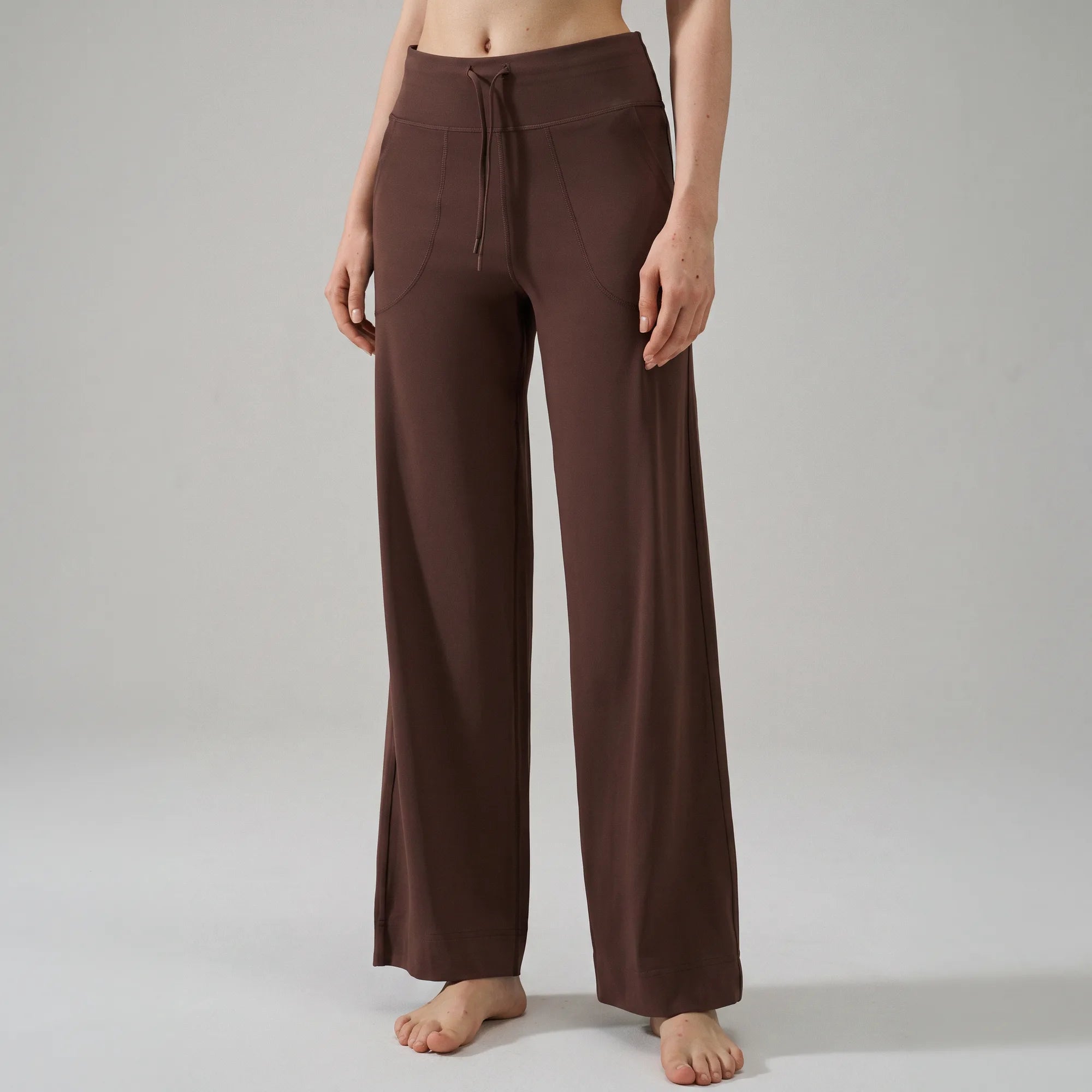 A model wearing brown wide-leg drawstring pants, shown from the waist down against a neutral light gray studio background.