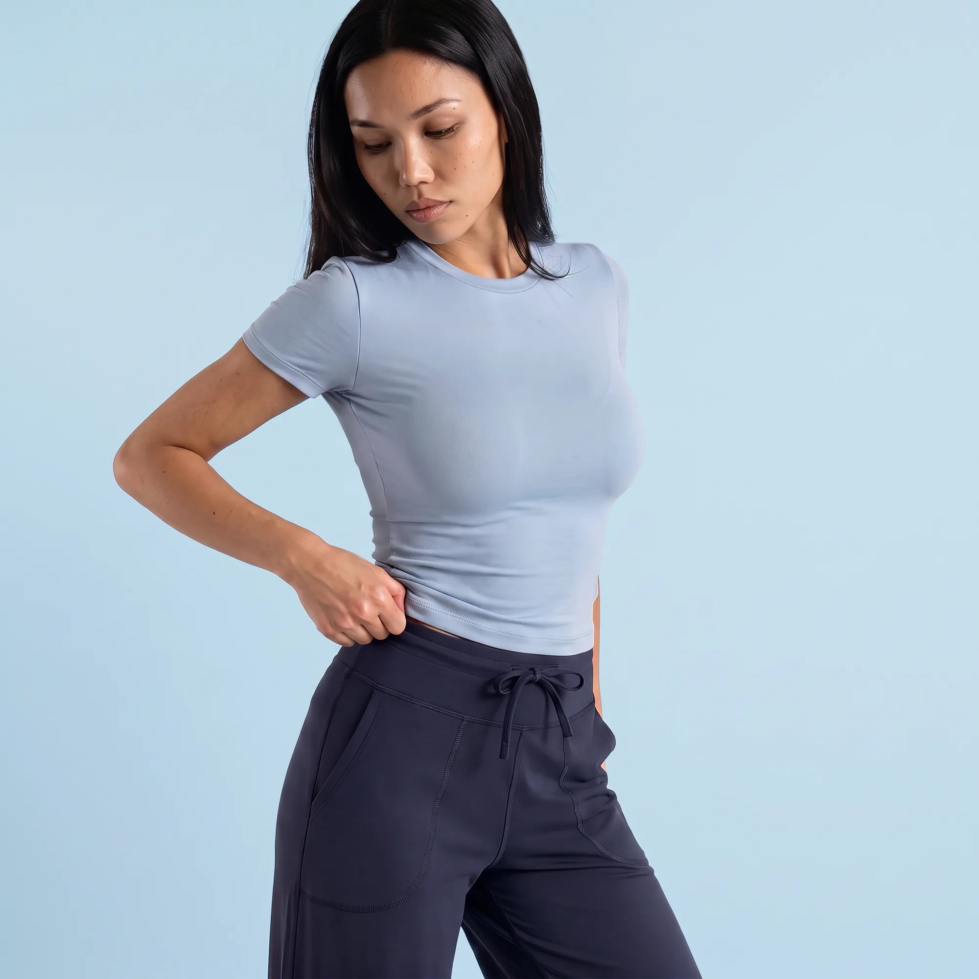 A woman modeling a light blue short-sleeve crewneck top and dark navy drawstring pants against a solid light blue background.