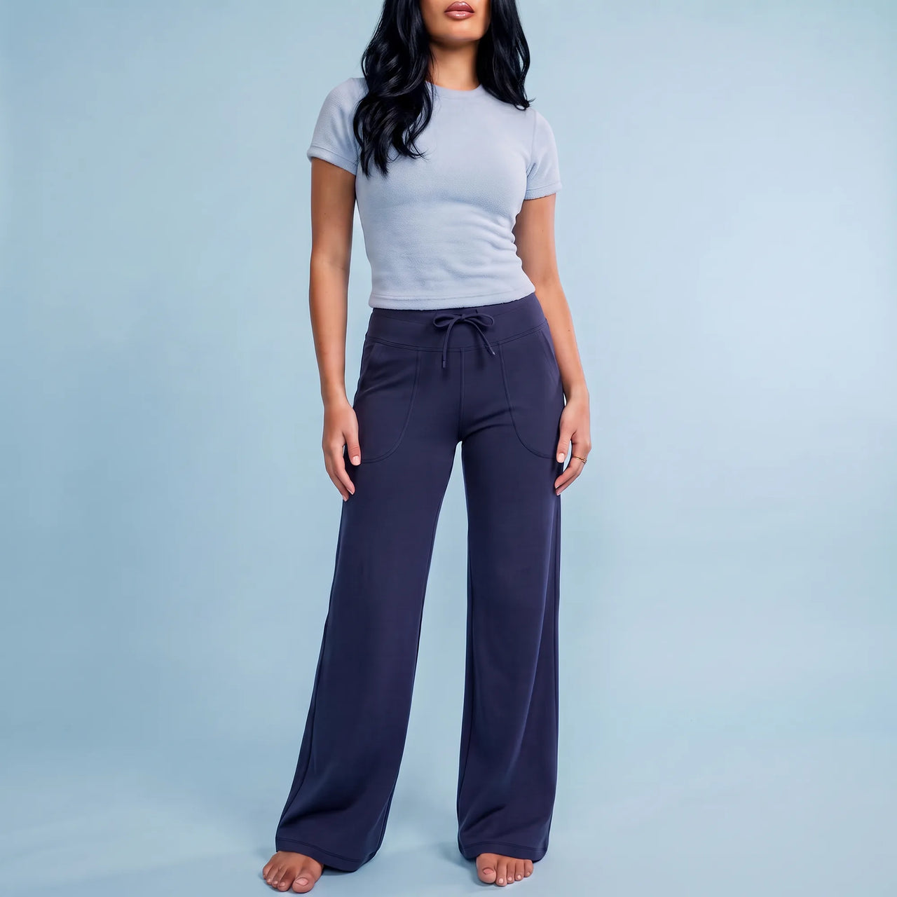 A woman modeling a light gray short-sleeve crewneck t-shirt and dark navy wide-leg drawstring pants against a solid light blue studio background.