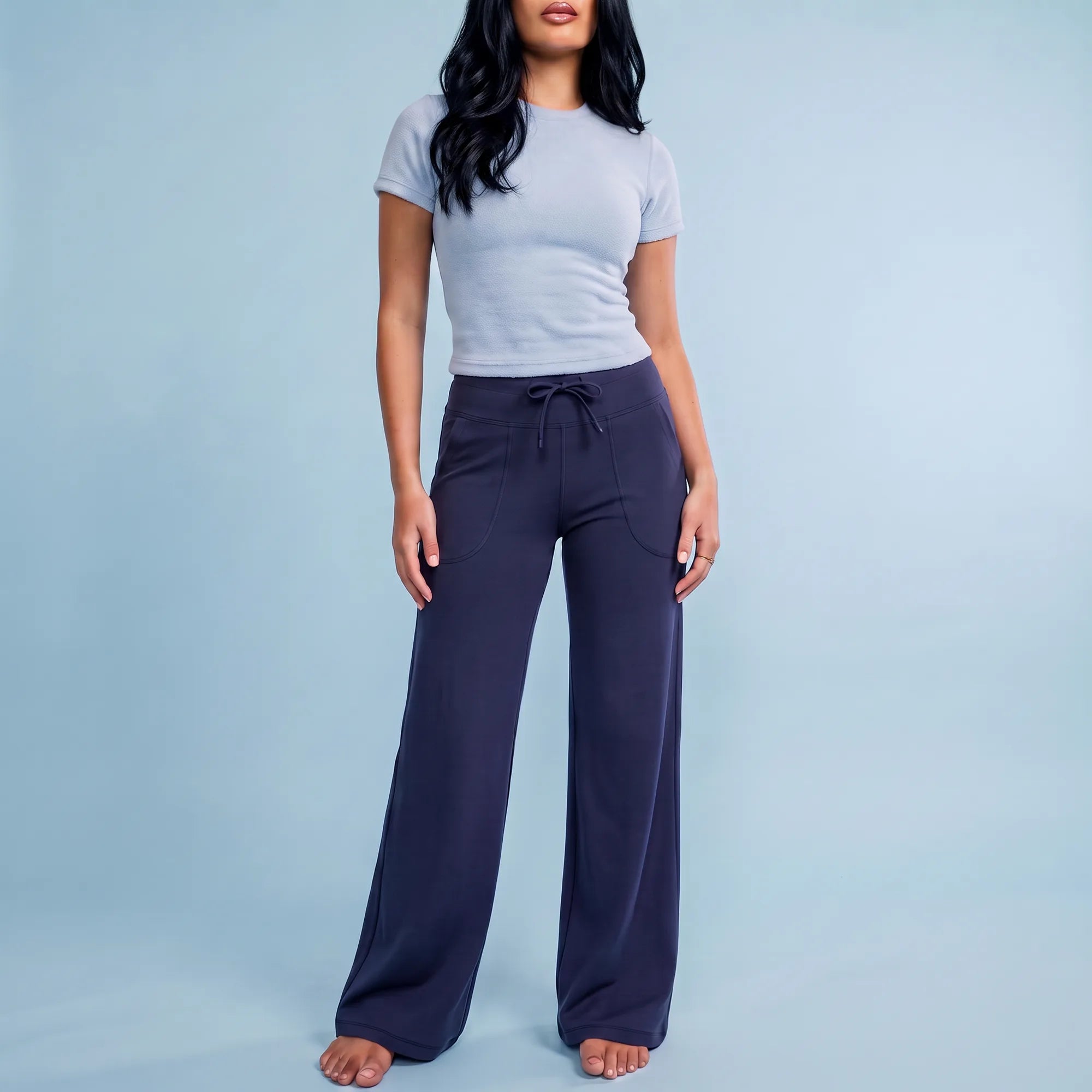 A woman modeling a light gray short-sleeve crewneck t-shirt and dark navy wide-leg drawstring pants against a solid light blue studio background.