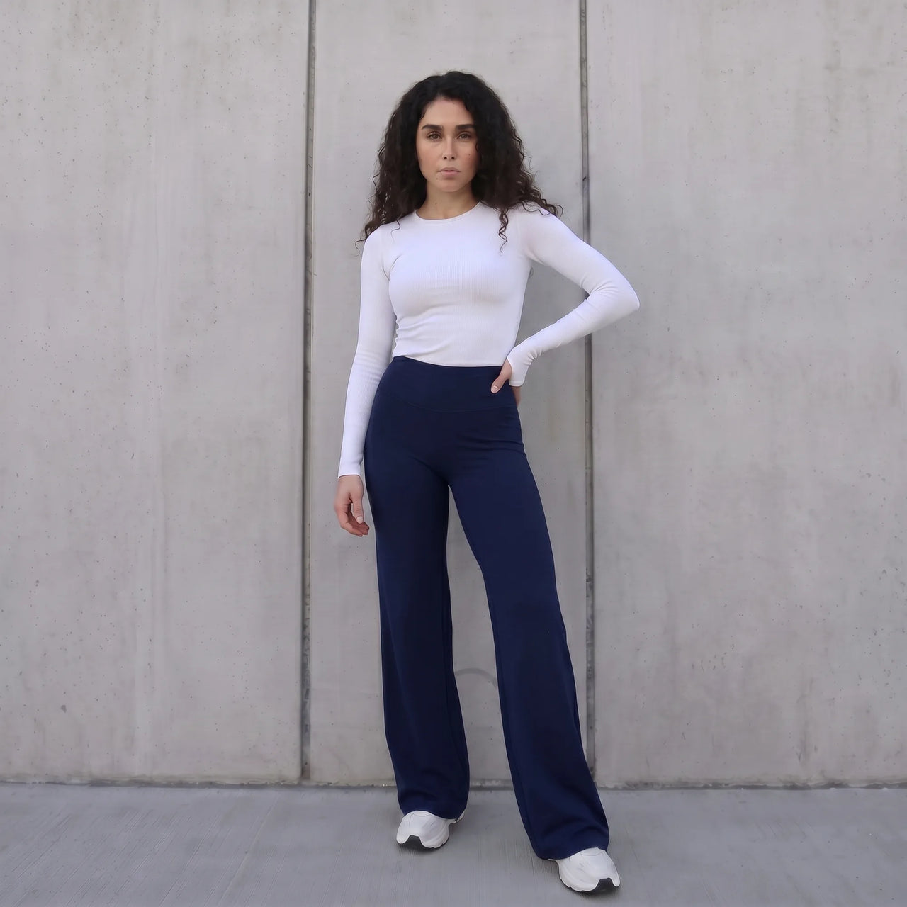 Woman wearing navy Pulso high-waisted wide-leg postpartum trouser styled with a white top, standing against a wall
