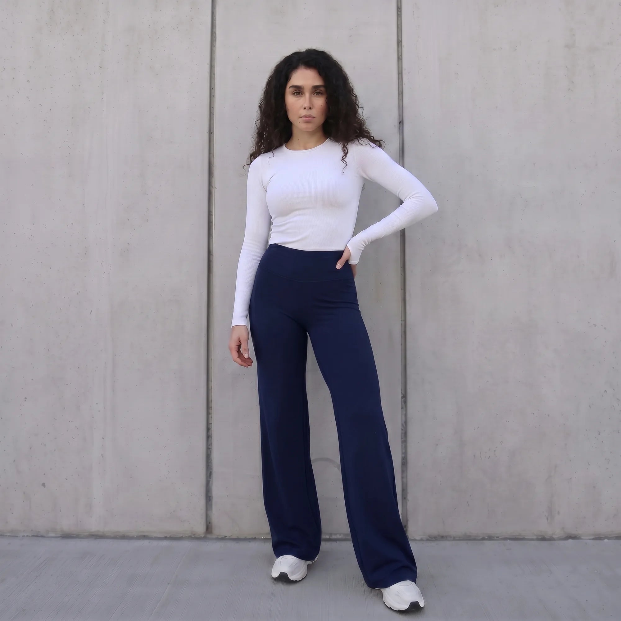 Woman wearing navy Pulso high-waisted wide-leg postpartum trouser styled with a white top, standing against a wall