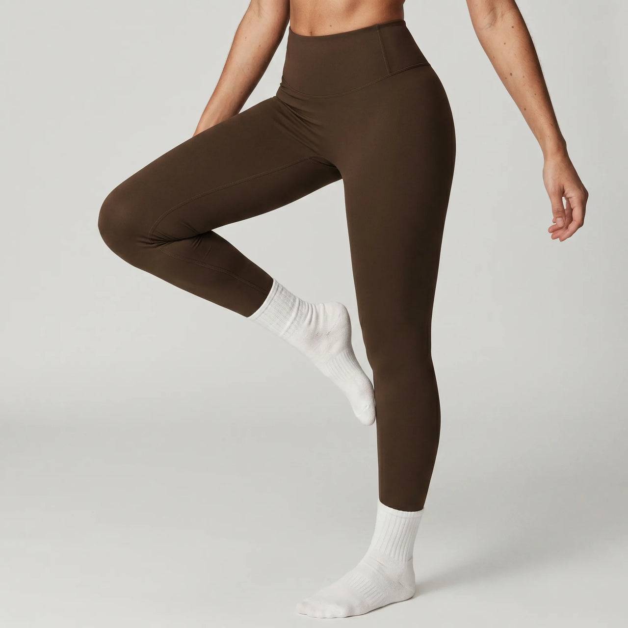 Woman wearing chocolate brown Retorno high-waisted postpartum legging, side view stretching