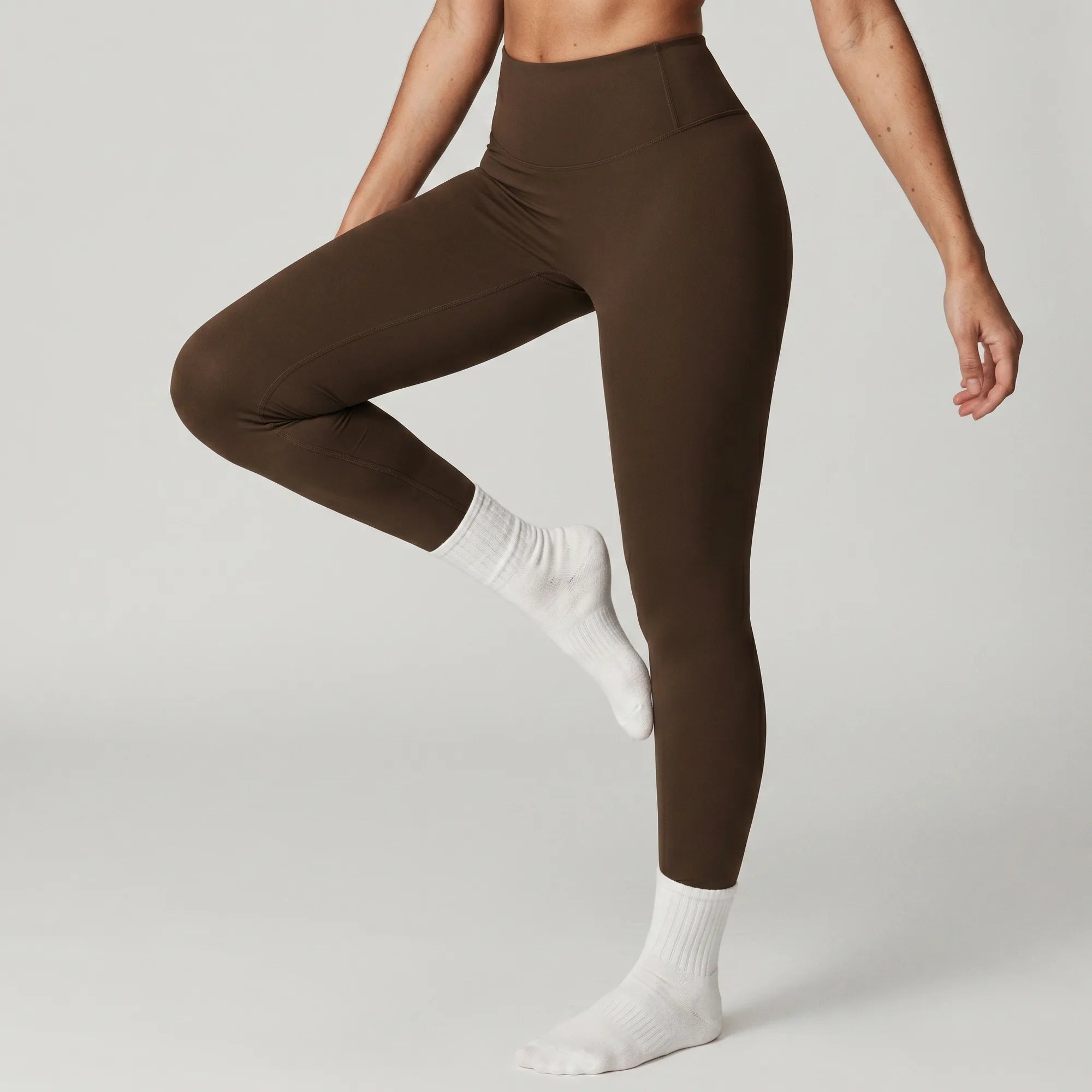 Woman wearing chocolate brown Retorno high-waisted postpartum legging, side view stretching