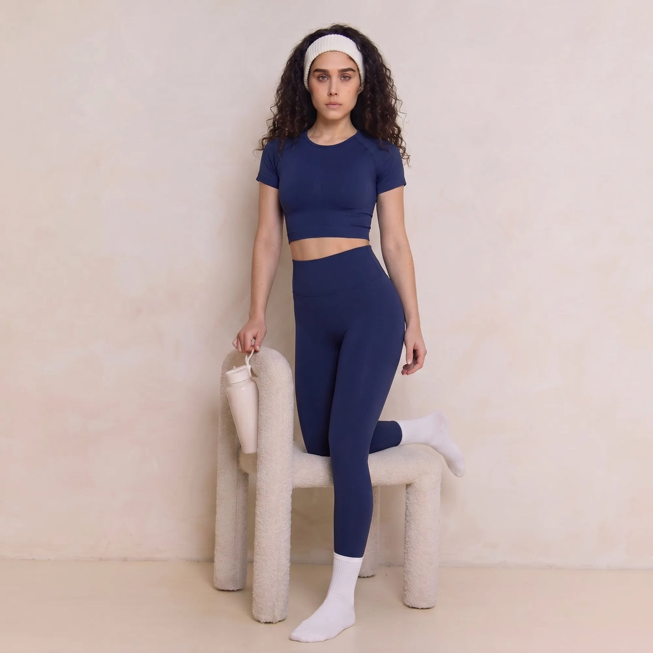 Woman wearing navy Retorno high-waisted postpartum legging, standing by chair
