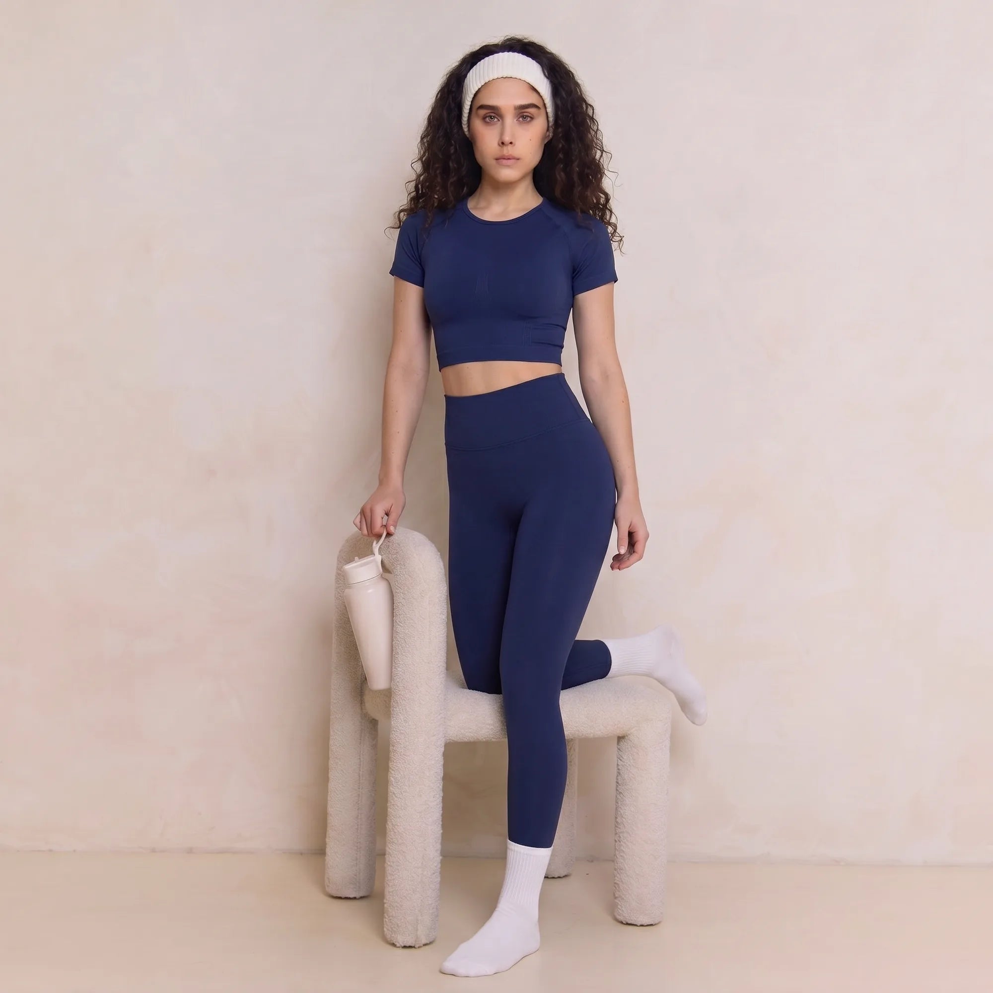 Woman wearing navy Retorno high-waisted postpartum legging, standing by chair
