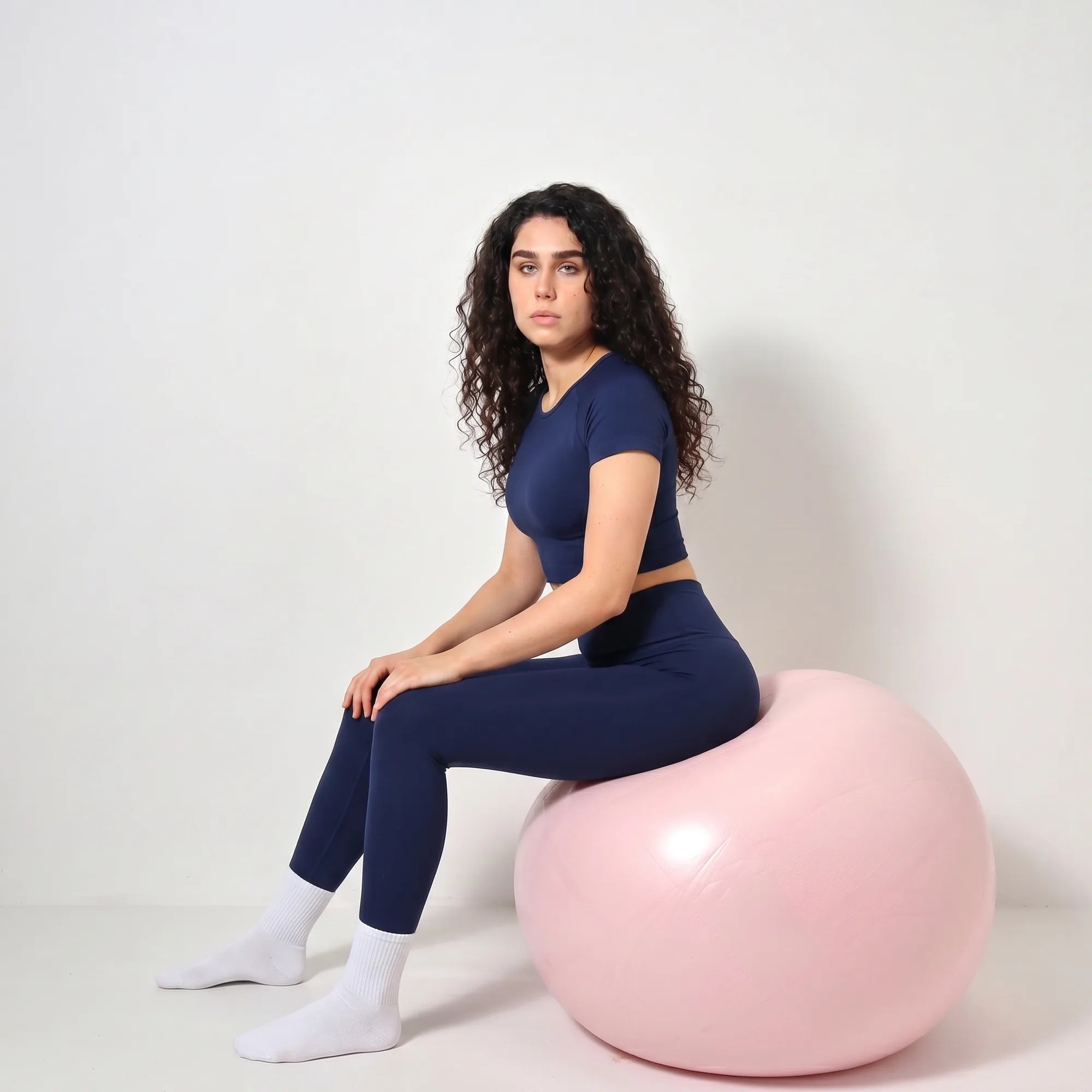 Woman wearing navy Retorno high-waisted postpartum legging, seated