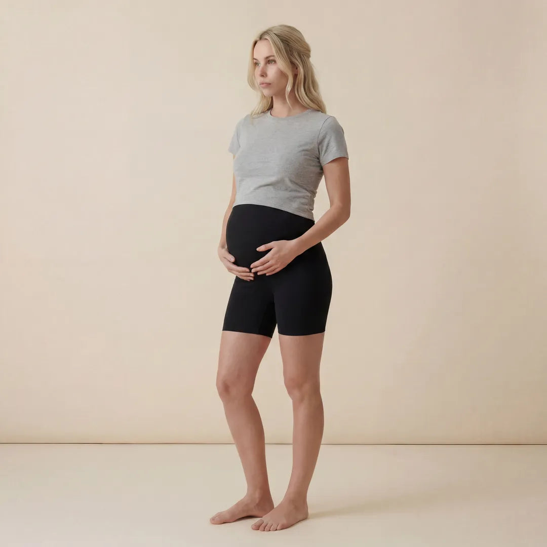 Woman wearing a gray t-shirt and black shorts standing against a beige background
